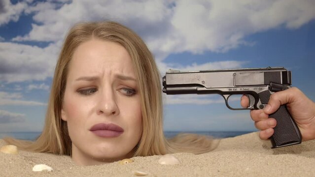 Woman buried in sand on beach with gun at her