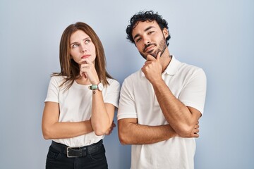 Young couple wearing casual clothes standing together looking confident at the camera smiling with crossed arms and hand raised on chin. thinking positive.