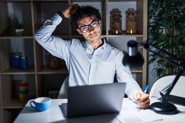 Hispanic man working at the office at night confuse and wondering about question. uncertain with...