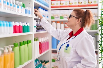 Young beautiful plus size woman pharmacist smiling confident holding product on shelving at pharmacy