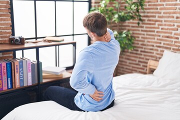 Young caucasian man suffering for back injury sitting on bed at bedroom