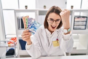 Young caucasian doctor woman holding canadian dollars banknotes annoyed and frustrated shouting with anger, yelling crazy with anger and hand raised