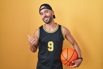 Middle age bald man holding basketball ball over yellow background pointing to the back behind with...