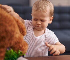 Adorable toddler playing with teddy bear and crying at home