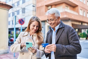 Middle age man and woman couple using smartphone and credit card at street