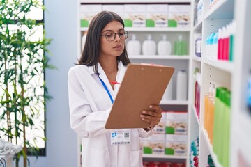 Young beautiful hispanic woman pharmacist writing on document at pharmacy