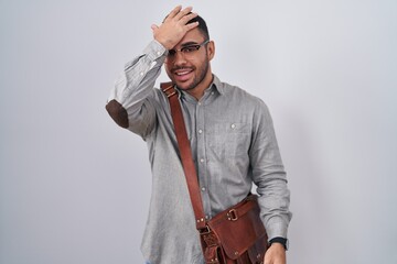 Young hispanic man wearing suitcase surprised with hand on head for mistake, remember error. forgot, bad memory concept.