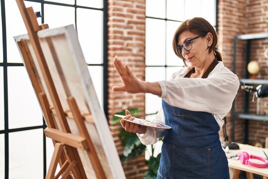 Middle age woman artist looking draw with doubt expression at art studio