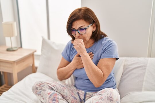 Middle age woman sitting on bed coughing at bedroom - Powered by Adobe