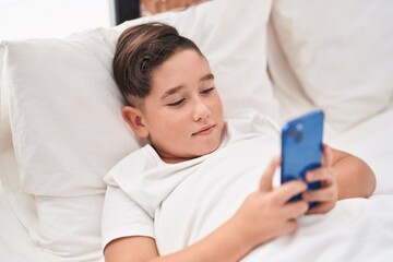 Obraz na płótnie Canvas Adorable hispanic boy using smartphone lying on bed at bedroom