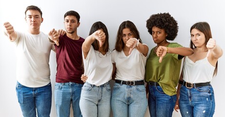 Group of young friends standing together over isolated background looking unhappy and angry showing rejection and negative with thumbs down gesture. bad expression. © Krakenimages.com