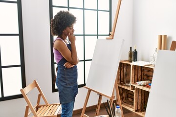 Young african american woman with doubt expression looking canvas at art studio