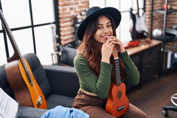 Young hispanic woman musician holding ukelele at music studio