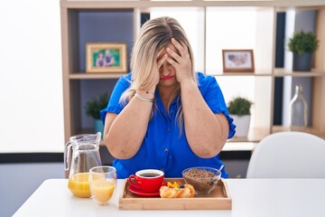Obraz na płótnie Canvas Caucasian plus size woman eating breakfast at home with sad expression covering face with hands while crying. depression concept.
