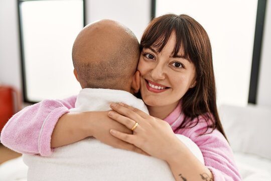 Young hispanic couple smiling happy and hugging wearing marriage ring at bedroom.