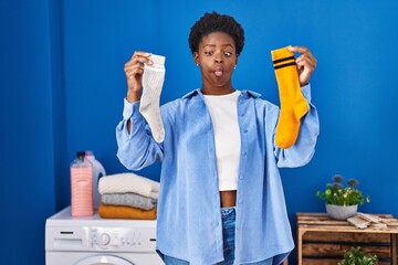African american woman holding clean andy dirty socks making fish face with mouth and squinting...