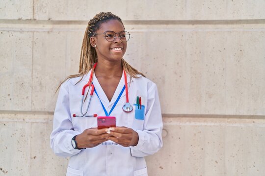 African american woman doctor smiling confident using smartphone at hospital