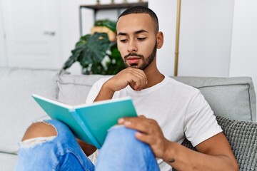 Young hispanic man reading book at home