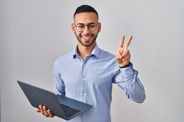 Young hispanic man working using computer laptop smiling looking to the camera showing fingers...