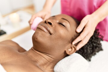 Obraz na płótnie Canvas African american woman lying on massage table having facial treatment at beauty salon