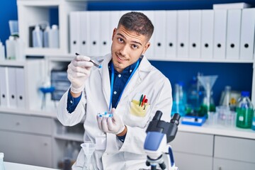 Young hispanic man scientist holding pills at laboratory