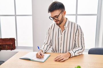 Young hispanic man business worker writing on notebook at office