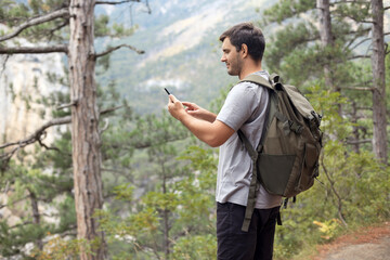 Hiker man walks in the mountain forest and using his phone at the background landscape with woods,  looking for connection