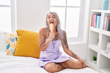 Middle age grey-haired woman singing song using brush as a microphone at bedroom