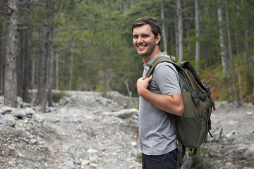 Portrait of happy smiling tourist man 30-35 years old with backpack hiking in national park
