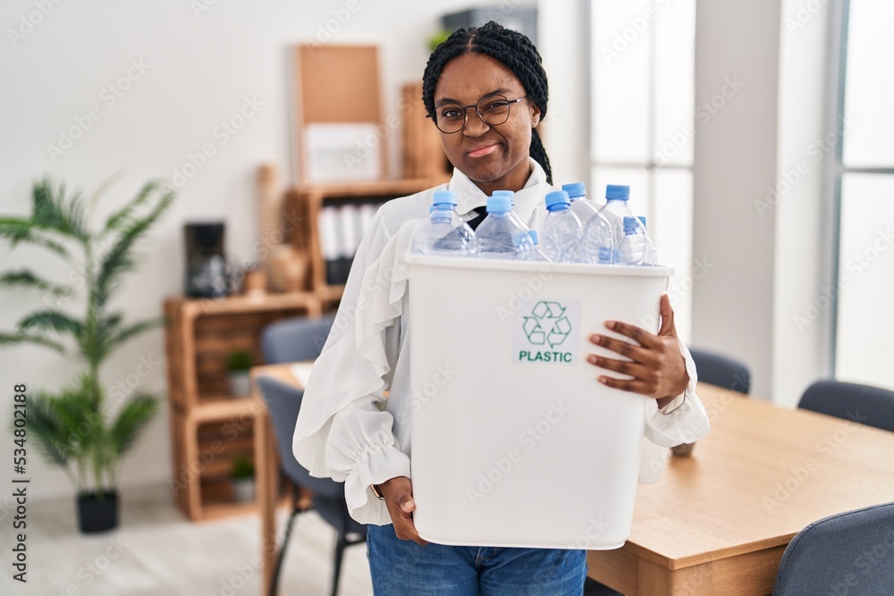 Wall mural African american woman working at the office holding plastic bottle for recycling skeptic and nervous, frowning upset because of problem. negative person.