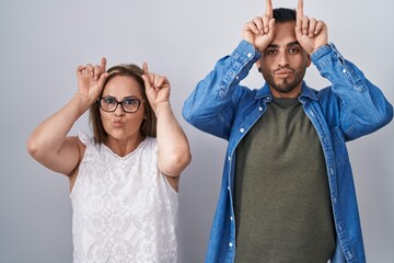 Hispanic mother and son standing together doing funny gesture with finger over head as bull horns