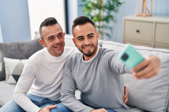 Two men couple make selfie by smartphone sitting on sofa at home