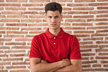 Young hispanic man standing over bricks wall skeptic and nervous, disapproving expression on face...