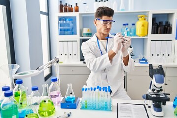 Young hispanic man wearing scientist uniform writing on test tube at laboratory