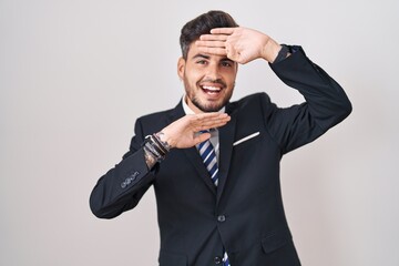 Young hispanic man with tattoos wearing business suit and tie smiling cheerful playing peek a boo with hands showing face. surprised and exited