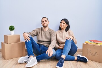 Young couple moving to a new home smiling looking to the side and staring away thinking.