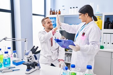 Man and woman wearing scientists uniform high five with hands raised up at laboratory