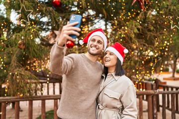Man and woman couple wearing christmas hat make selfie by the smartphone at park