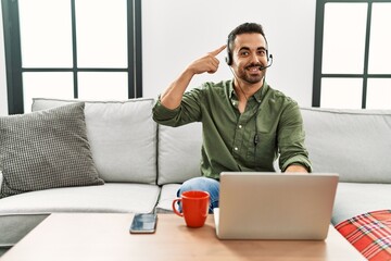 Young hispanic man with beard wearing call center agent headset working from home smiling pointing...
