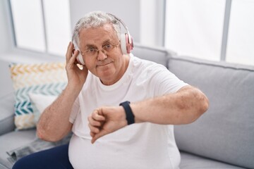 Middle age grey-haired man listening to music looking watch at home
