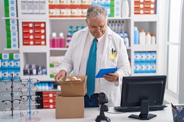 Middle age grey-haired man pharmacist using touchpad holding pills bottle at pharmacy