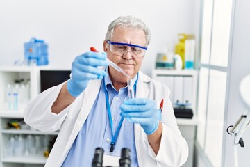 Middle age grey-haired man wearing scientist uniform using pipette at laboratory