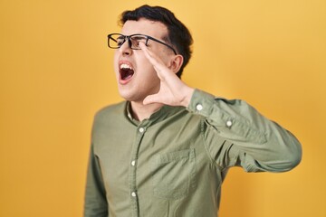 Non binary person standing over yellow background shouting and screaming loud to side with hand on mouth. communication concept.