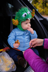 Tailgating baby monster is having some snacks in the back of the car on Halloween