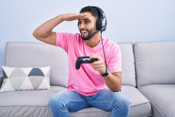 Hispanic young man playing video game holding controller sitting on the sofa very happy and smiling...