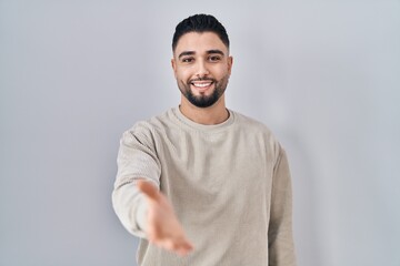 Fototapeta premium Young handsome man standing over isolated background smiling cheerful offering palm hand giving assistance and acceptance.