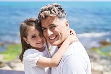 Father and daughter smiling confident hugging each other at seaside