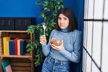 Fototapeta premium Young hispanic woman eating healthy whole grain cereals with spoon depressed and worry for distress, crying angry and afraid. sad expression.