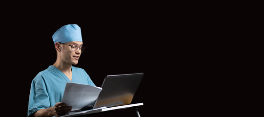 male doctor scientist speaks while looking into a laptop monitor on a dark background. The concept of online education and consultations in medicine