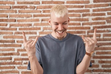 Young caucasian man standing over bricks wall shouting with crazy expression doing rock symbol with hands up. music star. heavy music concept.